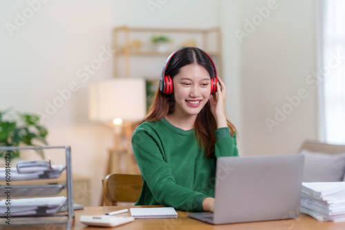 Free Download Cute Asian young woman wearing headphones using laptop computer at home. Asian woman using laptop, watching movie, listening to music, shopping online, watching live broadcast. - GFXLoad