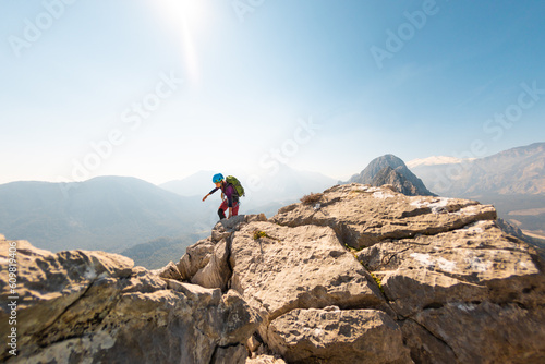 young girl climber in a helmet and with a backpack walks along a mountain range against the backdrop of mountains and climbing and hiking.