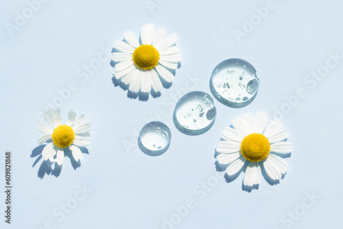 Chamomile flowers and drops of transparent liquid serum with bright light on a blue background. photo