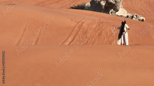 Young bearded man dressed as a shaman dancing on desert sand photo