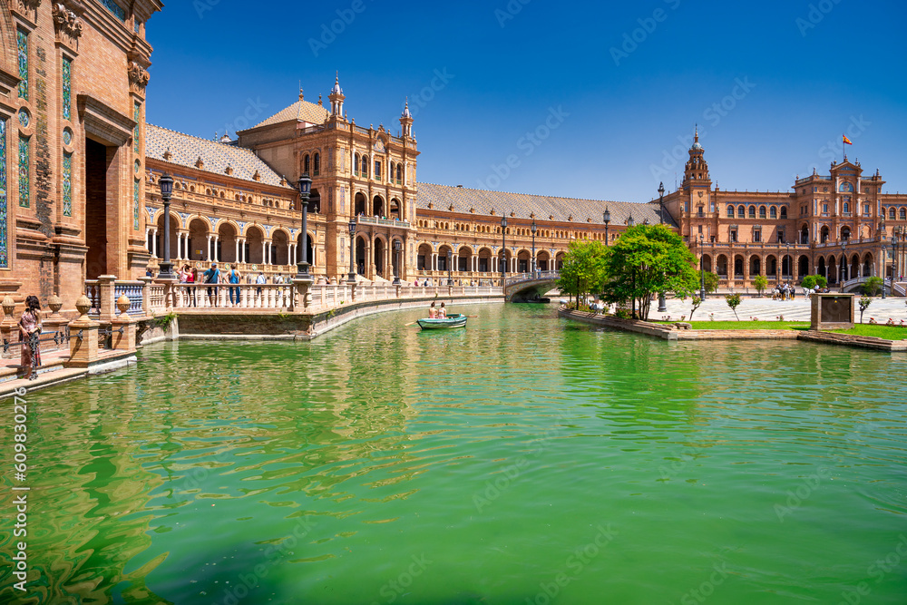 Sevilla, Spain - April 10, 2023: Several boats with people rowing at leisure on the lake of Plaza de Espana with buildings in the background