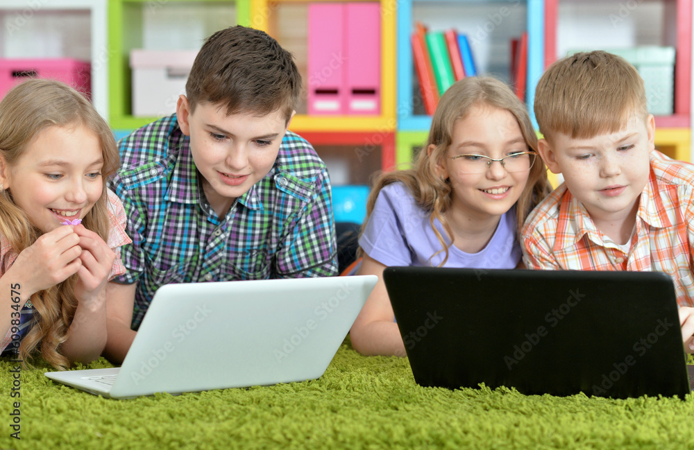 Children lying on floor with green carpet and looking at modern laptops Children lying on floor with green carpet and looking at modern laptops