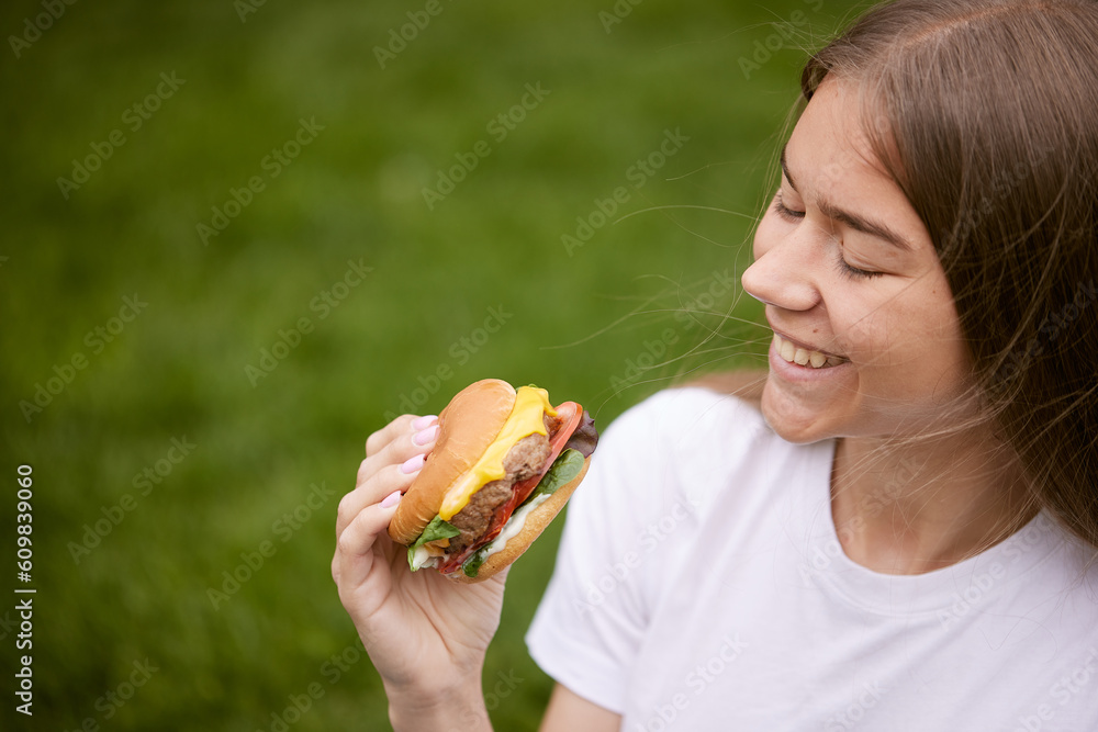 a young girl takes out a burger from a paper bag sitting on the green grass, the concept of food delivery, street food a young girl takes out a burger from a paper bag sitting on the green grass, the concept of food delivery, street food