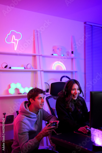 Couple streamer lover boy and girl use joystick for playing video game together hobby in the weekend at entertainment violet neon light room vertical style