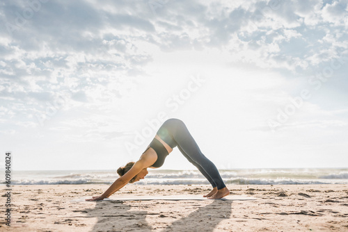 Woman practicing Adho mukha svanasana pose at beach photo