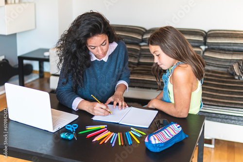 Freelancer mother guiding daughter drawing in notebook with laptop on table