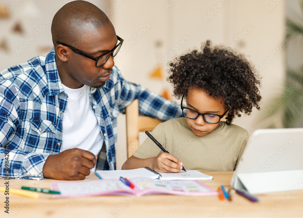 Naklejka premium Ethnic dad helps son to do homework at home.