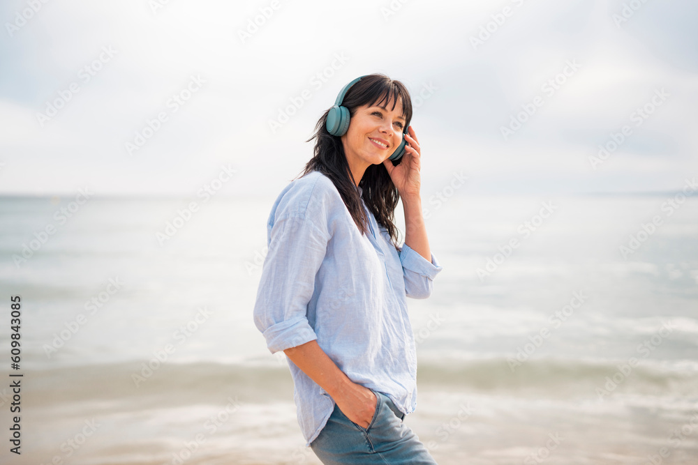 Smiling woman adjusting bluetooth headphones at beach Smiling woman adjusting bluetooth headphones at beach
