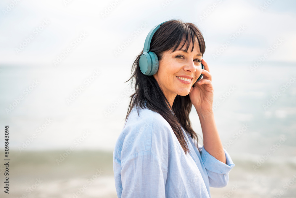 Smiling woman wearing wireless bluetooth headphones at beach Smiling woman wearing wireless bluetooth headphones at beach