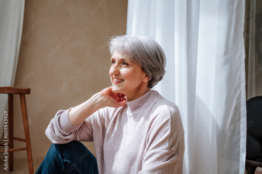 Thoughtful smiling woman sitting by curtain at home Thoughtful smiling woman sitting by curtain at home