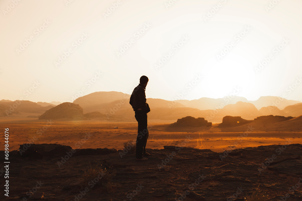 Young man standing in desert and looking at sunset Young man standing in desert and looking at sunset