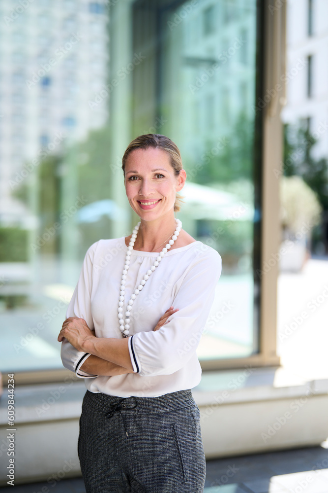 Smiling businesswoman standing with arms crossed in front of glass wall Smiling businesswoman standing with arms crossed in front of glass wall