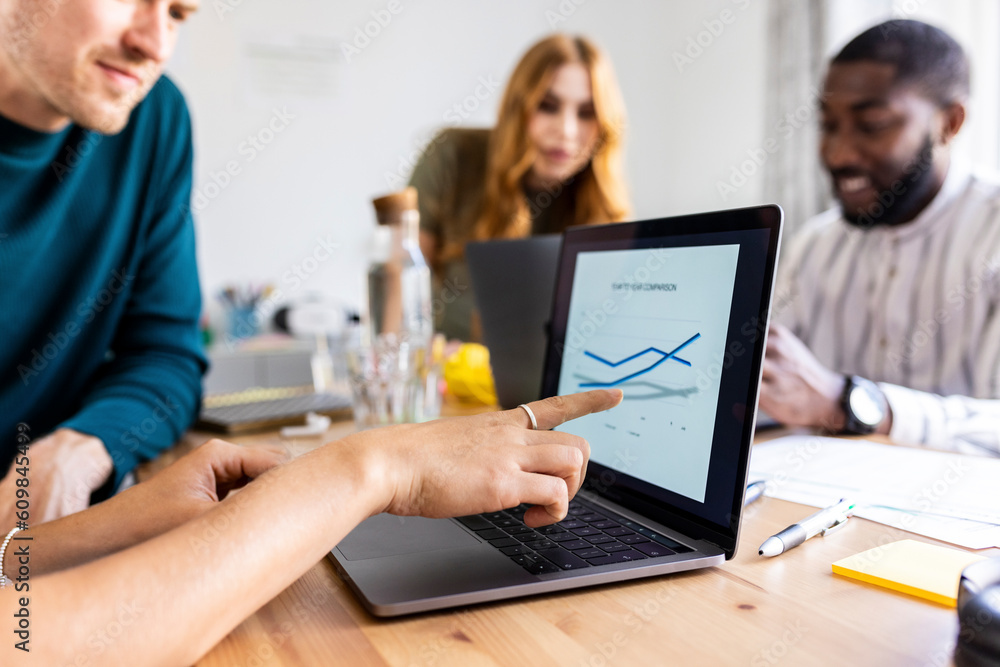 Businesswoman pointing at graph on laptop and planning strategy with colleagues in office Businesswoman pointing at graph on laptop and planning strategy with colleagues in office