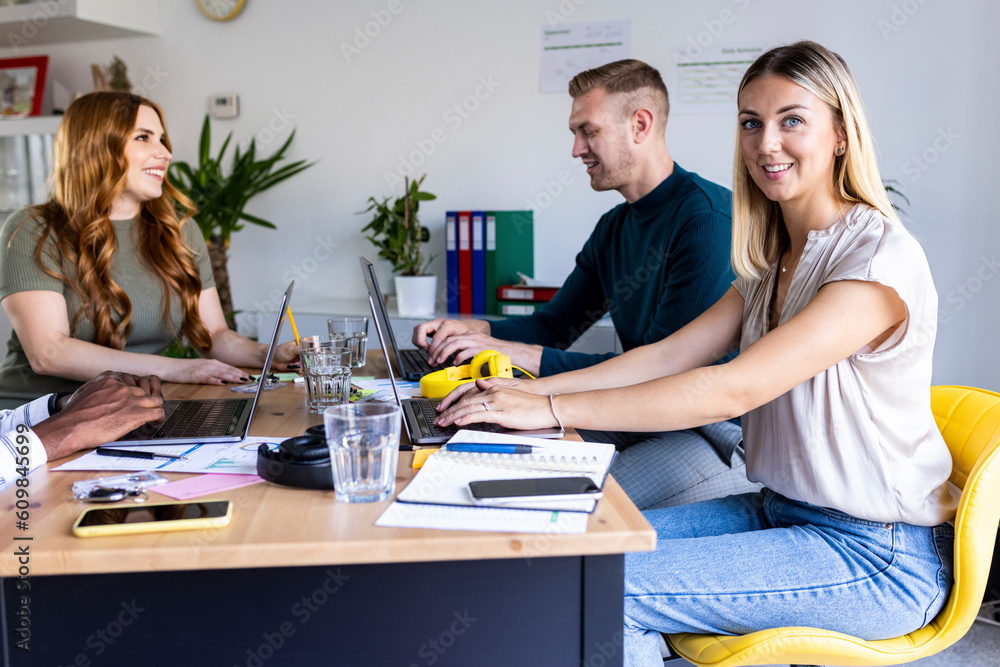 Smiling young businesswoman with laptop by colleague in office Smiling young businesswoman with laptop by colleague in office