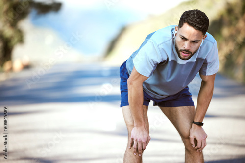 Fitness, man and tired outdoor with music on a run or workout with earphones. Male athlete person or runner listening to audio on a road for cardio training, running or exercise break to breathe
