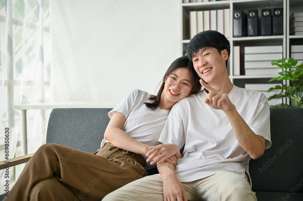 A cute young Asian girlfriend is hugging her boyfriend while enjoying watching TV on a couch