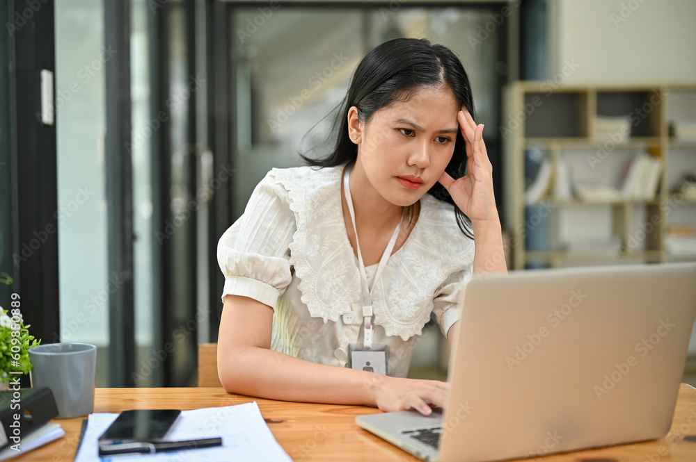 Stressed and serious Asian businesswoman looking at her laptop screen, working in her office. Stressed and serious Asian businesswoman looking at her laptop screen, working in her office.