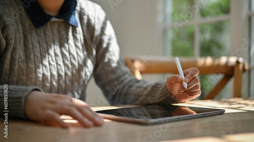Cropped image of a female in cozy sweater working on her tasks on her digital tablet