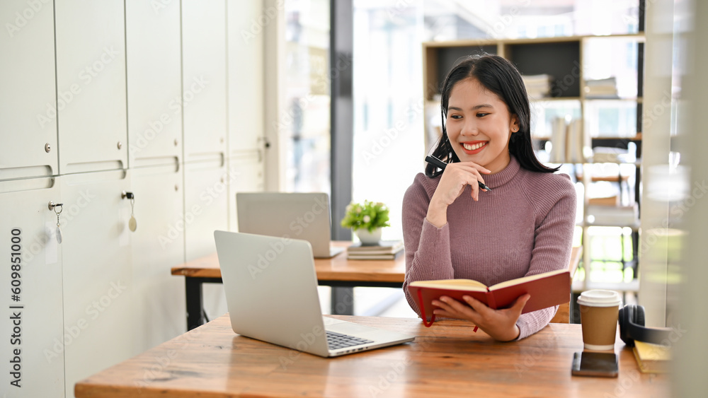 Happy Asian female college student looking her laptop screen, doing homework Happy Asian female college student looking her laptop screen, doing homework