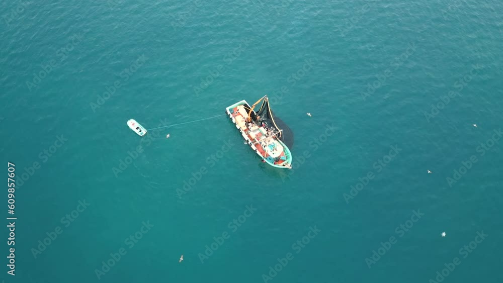 A thriving fishing trawler, surrounded by seagulls, hauls in a teeming net of fish from the expansive sea. A thriving fishing trawler, surrounded by seagulls, hauls in a teeming net of fish from the expansive sea.