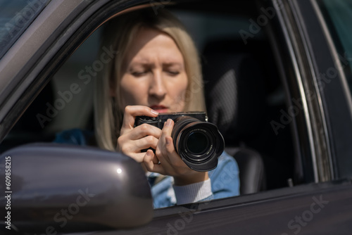 Woman with a camera sits in a car and takes pictures with a professional camera, a private detective or a paparazzi spy. Journalist is looking for sensations and follows celebrities.