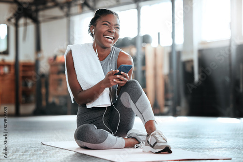 Phone, earphones and funny black woman in gym for fitness, sports or exercise. Smartphone, music and African female athlete laughing at web meme or comedy on break after workout, training or pilates.