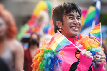 LGBTQ man having fun celebrate pride with flags at the annual Pride Parade, holding rainbow flags in two hands, celebrating LGBT pride month parade