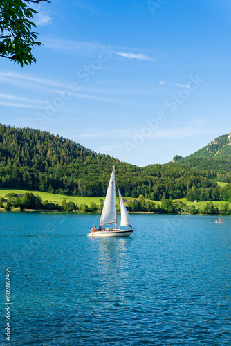 Sailing boat in the lake against the background of mountains and green forest. Sailboat floating on the water on a beautiful summer day with a clear blue sky. near St. Gilgen, Austria. 