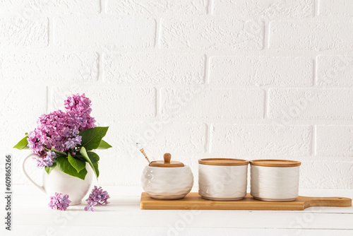 Beautiful kitchen background in light colors in a minimalist style. Three ceramic jars for storage on a wooden board and a bouquet of lilacs in a jug.