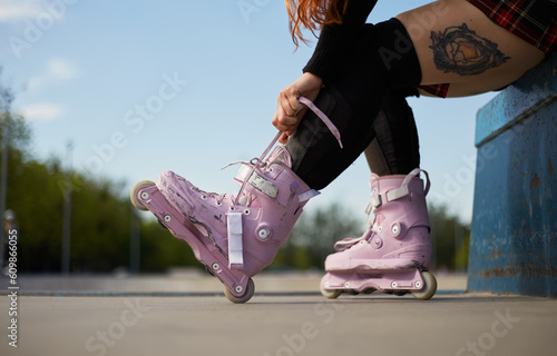 Aggressive inline skater girl tying laces on modern roller blades in a skatepark. Young female athlete preparing for a ride on skates