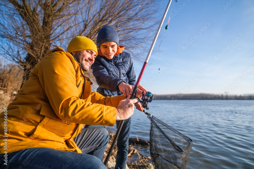 Obraz premium Father and son are fishing on sunny winter day. Freshwater fishing. Teenage boy is learning to fish.