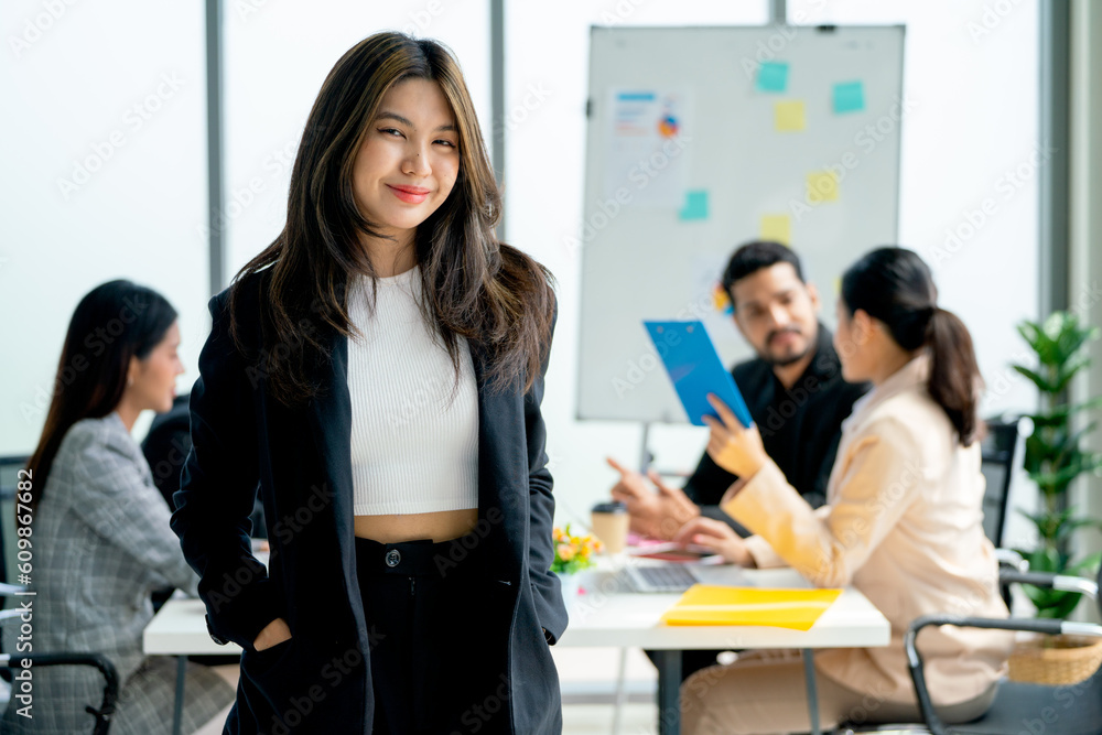 Portrait of Asian business woman stand with relax position and look at camera in front of other co-workers discuss on the back in office. Portrait of Asian business woman stand with relax position and look at camera in front of other co-workers discuss on the back in office.