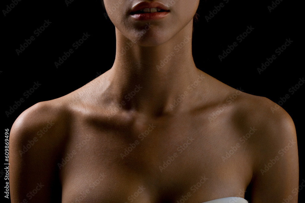 Fototapeta premium Bust of a woman, focusing on the neck and shoulders, frontal view, natural skin, lighting with shadows, definition of the collarbones and neck muscles, natural model on black background