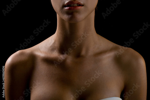Bust of a woman, focusing on the neck and shoulders, frontal view, natural skin, lighting with shadows, definition of the collarbones and neck muscles, natural model on black background