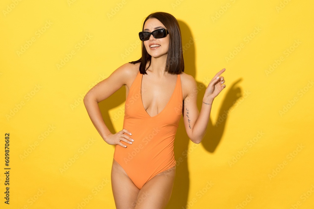 Summer vacation advertising.Young woman's alluring swimsuit and chic sunglasses are perfectly complemented by the sunny yellow background