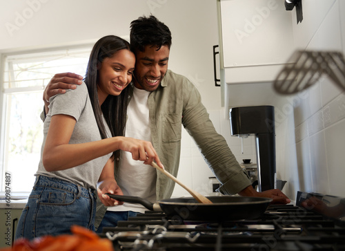 Happy young biracial couple in casual clothing cooking food in saucepan over stove in kitchen