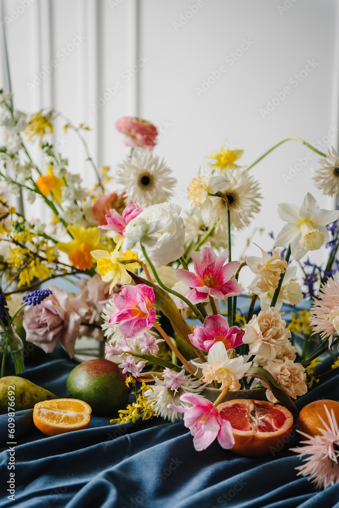 Festive decorated with flowers, fruits, greenery, candles. Beautiful bouquet in vase, orange, pear, pomelo, grapefruit on table. Home interior with decor elements. Summer composition of garden flowers