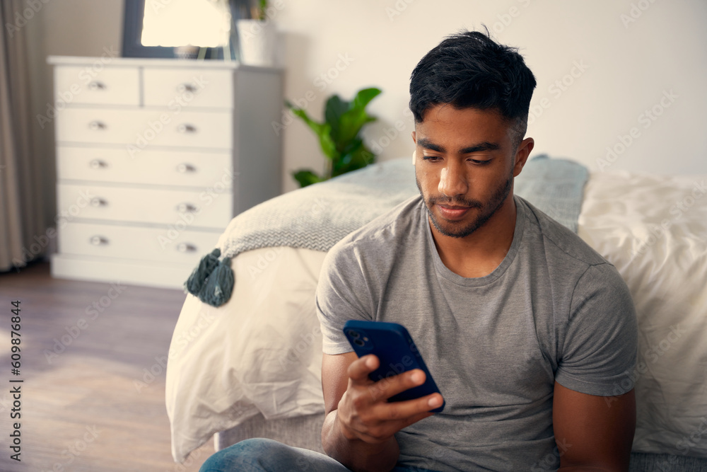 Young biracial man in casual clothing using mobile phone in bedroom at home Young biracial man in casual clothing using mobile phone in bedroom at home