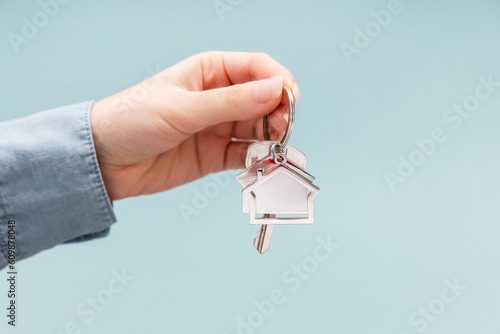 Female hand holding key and house keychain. Light blue background with copy space. Concept of mortgage, leasing of real estate