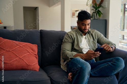 Young biracial man in casual clothing sitting on sofa using mobile phone at home © StratfordProductions