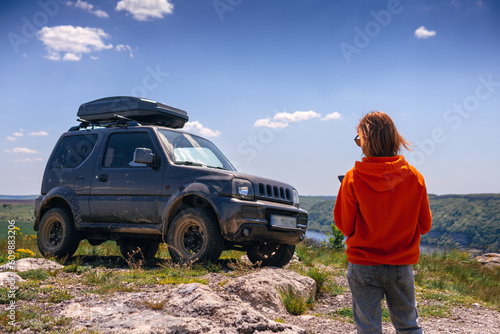 Portrait of a woman posing in sunglasses and an orange sweater. Off-road car with roof rack on background. travel and adventure. Active tourism. mountain activities. Car trip.