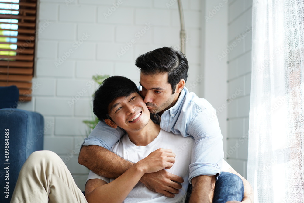 Obraz premium Romantic LGBTQ couple embracing from the back, sitting together at home. Diversity of LGBT relationships. A gay couple living together concept