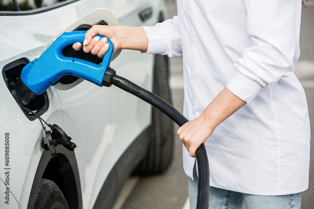Young business woman refueling her electric car at a EV charging station. Concept of environmentally friendly vehicle. Electric car concept. Green travelling.