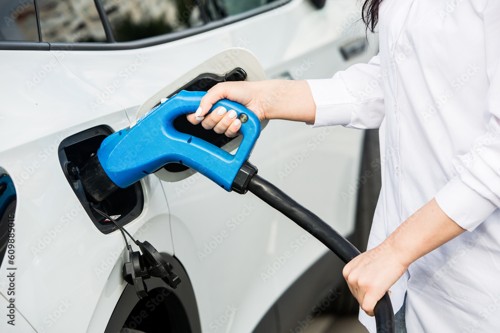 Young business woman refueling her electric car at a EV charging station. Concept of environmentally friendly vehicle. Electric car concept. Green travelling. Young business woman refueling her electric car at a EV charging station. Concept of environmentally friendly vehicle. Electric car concept. Green travelling.