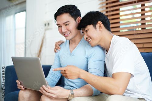 Gay Couple Using Computer For Video Conference On Sofa. Diversity of LGBTQ relationships. A gay couple living together concept