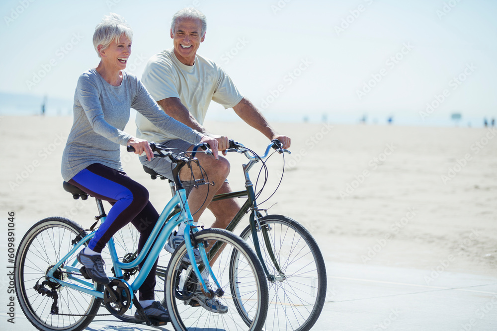 Senior couple riding bicycles on beach boardwalk