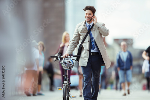 Businessman talking on cell phone pushing bicycle in city