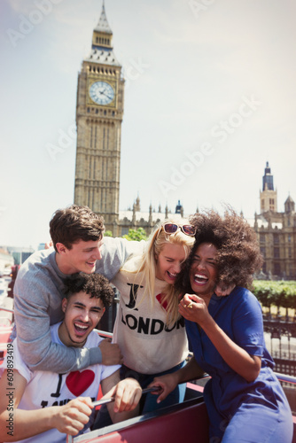Enthusiastic friends riding double-decker bus below Big Ben clocktower, London, United Kingdom photo