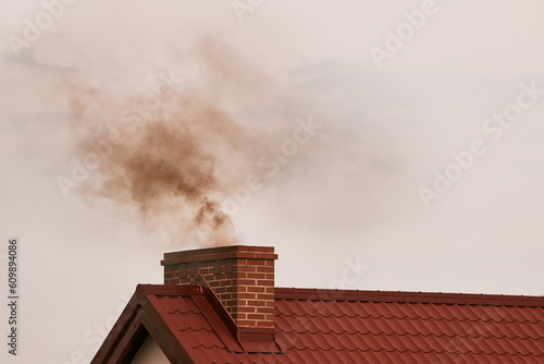 Black smoke comes out of a modern house chimney. The concept of global warming and environmental pollution. Heating with solid fuel.