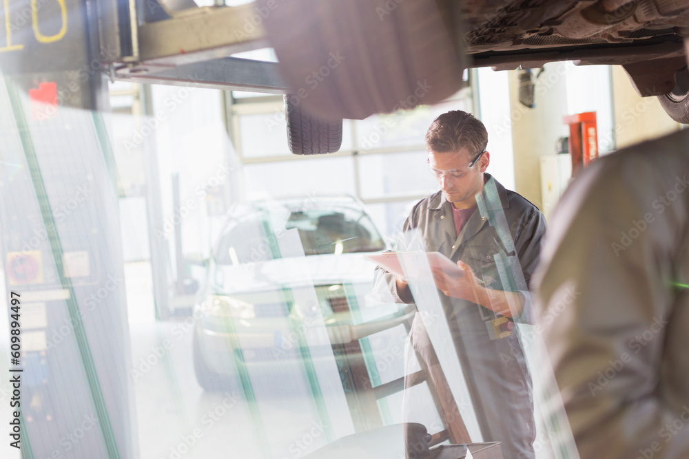 Fototapeta premium Mechanic with clipboard under car in auto repair shop